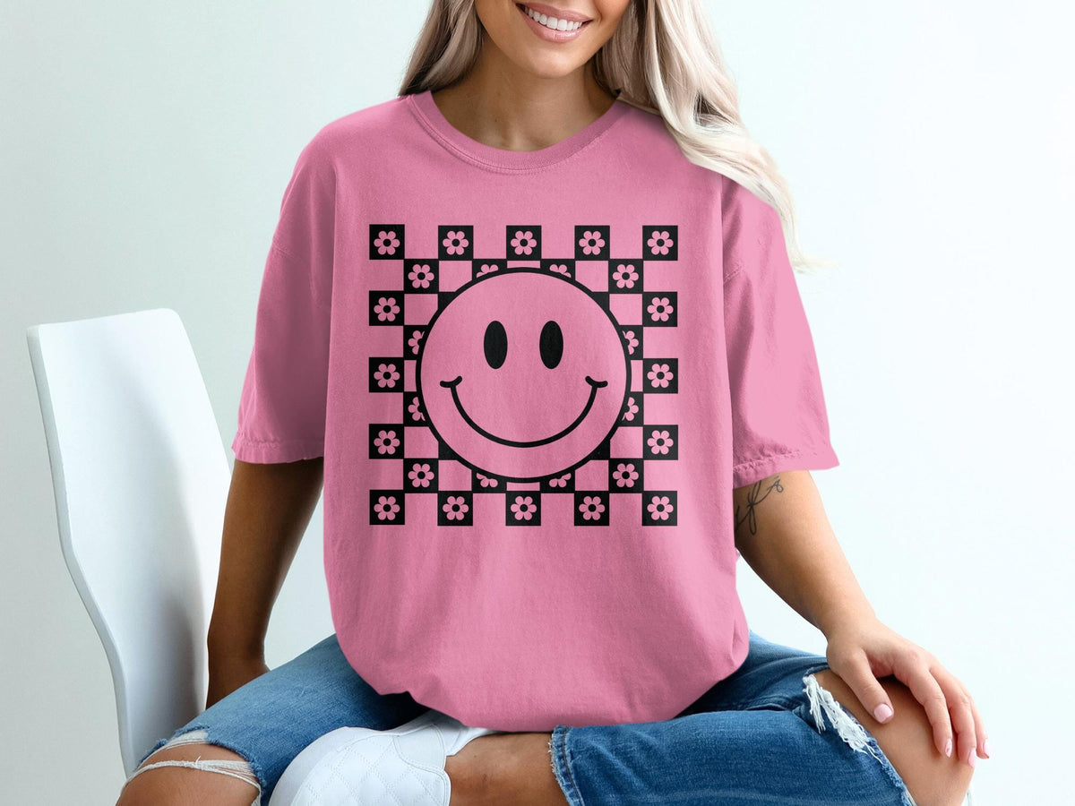 Pink t-shirt with black smiley face and flower checkerboard graphic.