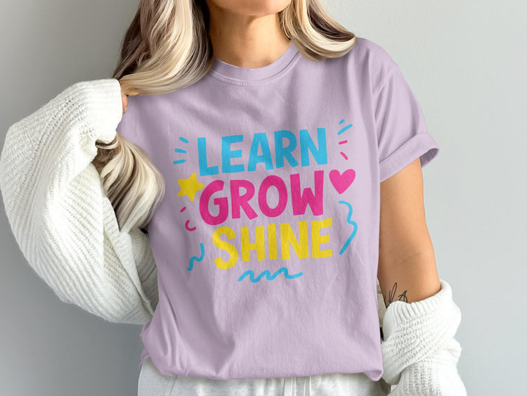 Lilac t-shirt with "LEARN GROW SHINE" text in bright blue, pink, and yellow.