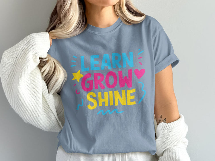 Gray t-shirt with "LEARN GROW SHINE" text in bright colors and graphic accents.