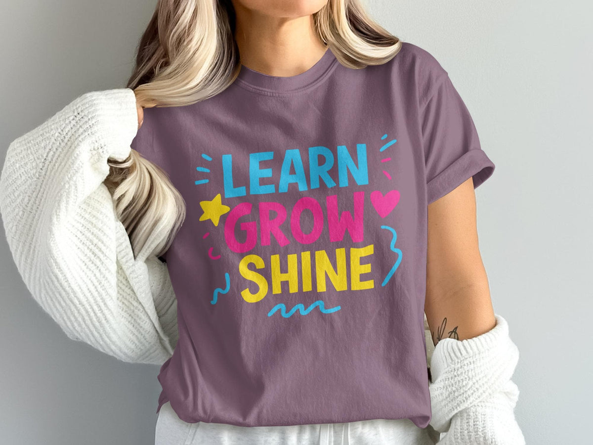 T-shirt with "LEARN GROW SHINE" text in blue, pink, and yellow, decorated with stars and hearts.