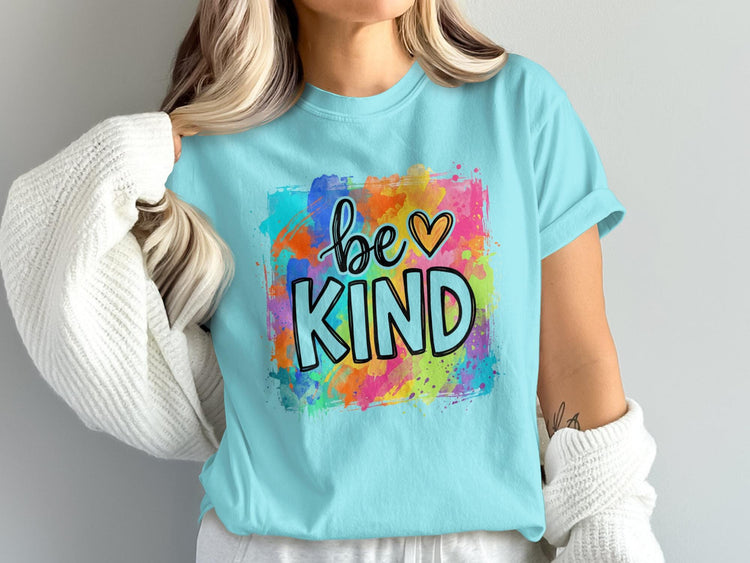 Light blue t-shirt with "be KIND" text in black outline on a colorful paint splash background.