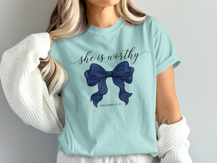 Light blue t-shirt with "she is worthy" and a navy bow, Proverbs 31:25.