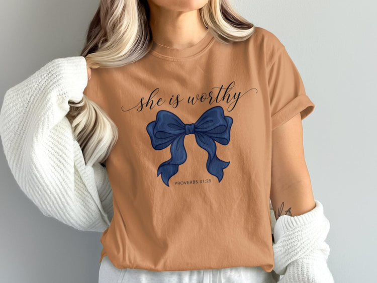 Tan t-shirt with navy bow and "she is worthy" text, PROVERBS 31:25.