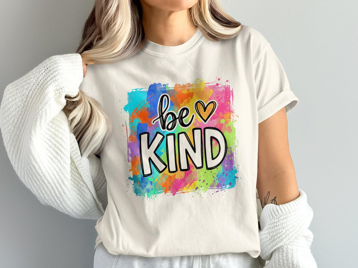 Cream t-shirt with "be KIND" text over colorful watercolor splashes.