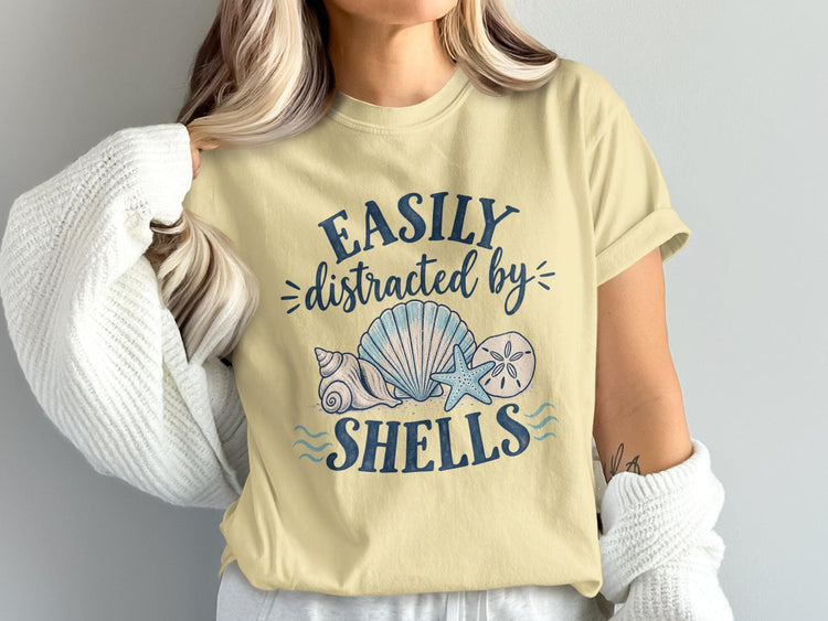 Pale yellow t-shirt with "Easily distracted by shells" and beach graphic.