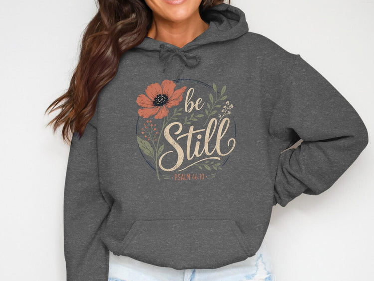 Dark grey hoodie with "be still" and "Psalm 46:10" in floral circle graphic.