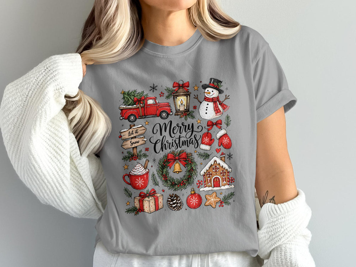 Merry Christmas graphic with truck, snowman, gingerbread house, and gifts on gray t-shirt.